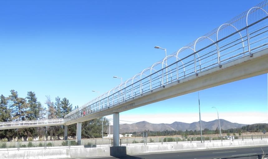 Pasarela peatonal de hormigón con barandas metálicas sobre una autopista